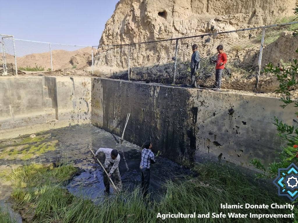 People clearing muddy water from a reservoir, with children observing, representing agricultural and safe water improvement projects funded by crypto donations like ETH.