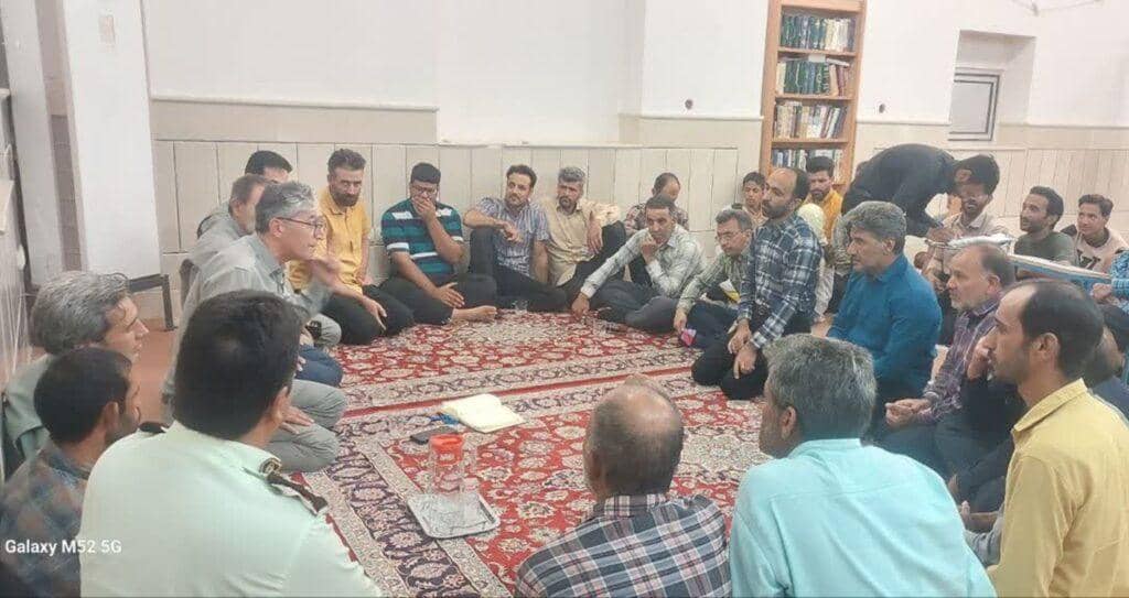 Diverse individuals gathered on a carpeted floor, listening attentively to a speaker, possibly a community meeting focused on sadaqah jariyah projects funded by crypto donations like BTC.