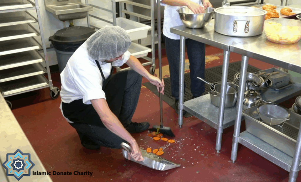 A volunteer cleans a kitchen floor where chopped carrots have fallen, symbolizing the essential but often unseen work of charitable operations funded by crypto donations like BTC.
