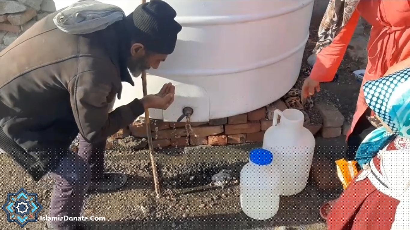 Man collecting water from a spigot on a large white tank, helping provide clean water for families. Supported by crypto donations like USDT on Trc20.