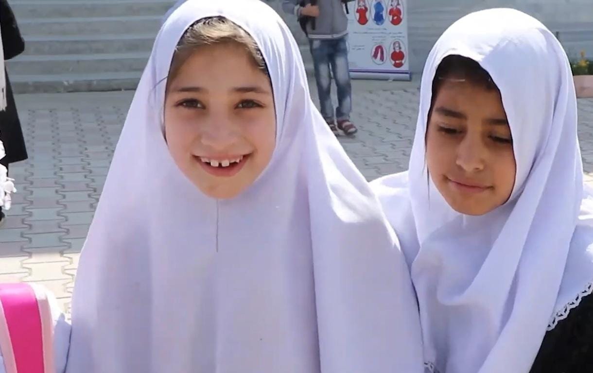 Two young girls in white hijabs smiling, representing the impact of IslamicDonate.Com's crypto Khums donations, supporting education for orphans. Funds are processed via Arab Emirates Dirham.