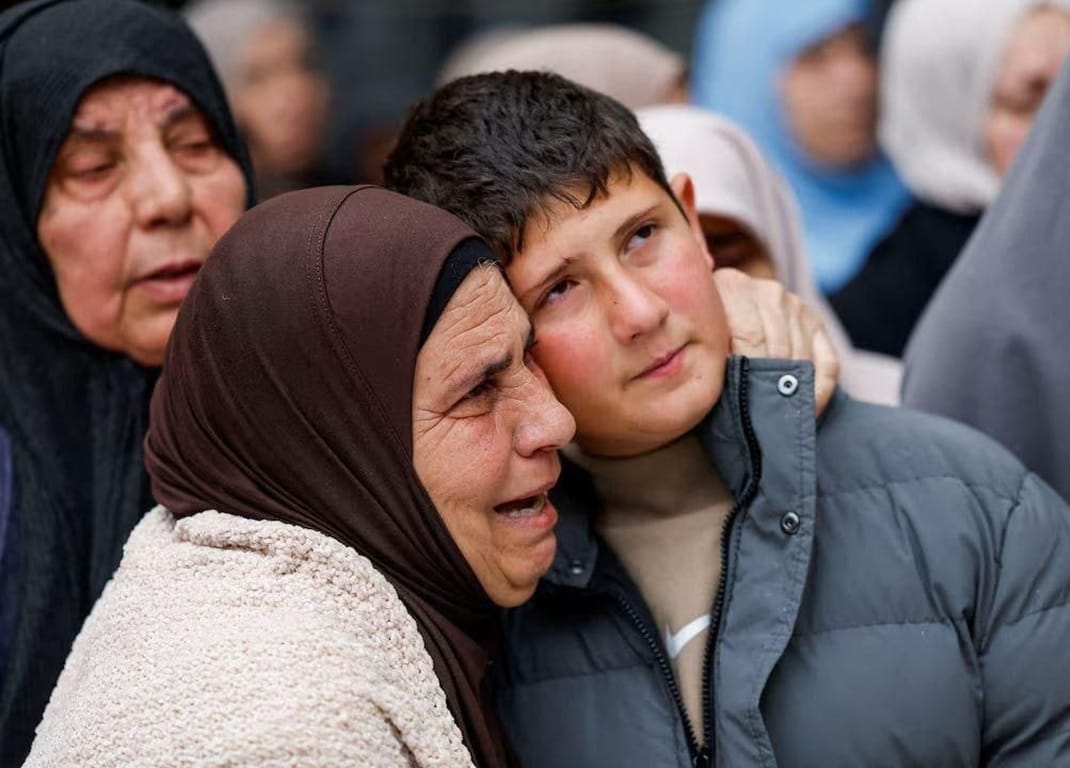 Middle-aged woman crying as a young man embraces her, with others in background. Daily Sadaqah with cryptocurrency donation for families in need, using BNB or XRP.