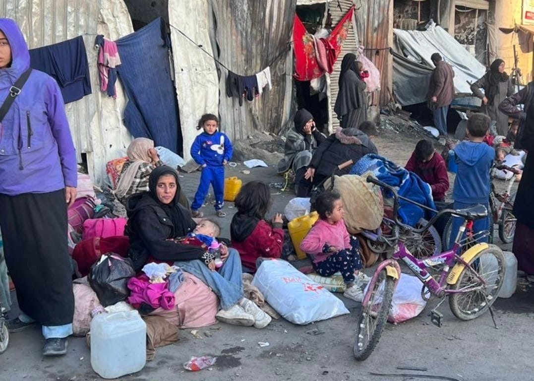 Displaced families with children gather belongings, with a young girl in blue overalls standing. Donation for today provisions help, such as meals, toys, and care, facilitated by crypto like SOL.