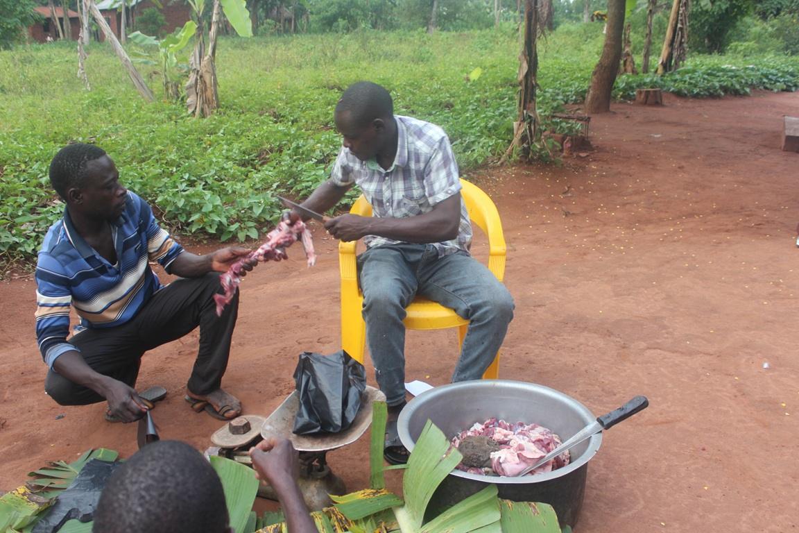 Two men preparing meat for distribution, one seated and cutting, the other holding a piece, with a large bowl of meat ready. Crypto donations like Bitcoin enable this charitable work, feeding families globally.