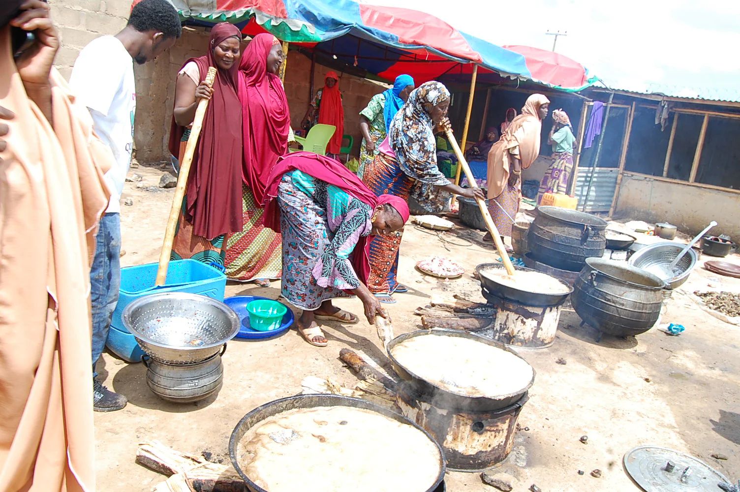 Women are preparing large communal meals of hot food during Eid al-Adha, made possible by crypto donations, including ETH. They are stirring huge pots over open fires, symbolizing the distribution of sustenance and spreading joy.