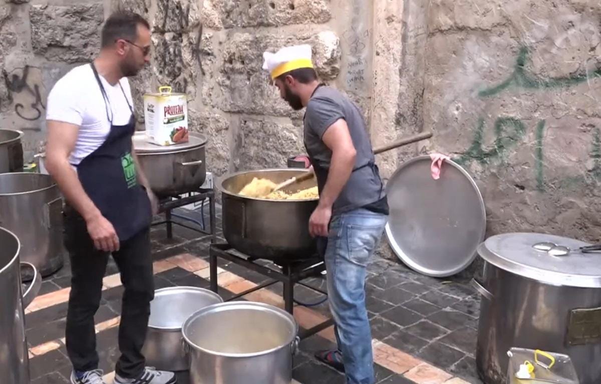 Two men prepare large pots of food in an outdoor setting, likely for charity. This scene illustrates fidya payment for Ramadan, with aid supported by Ethereum.