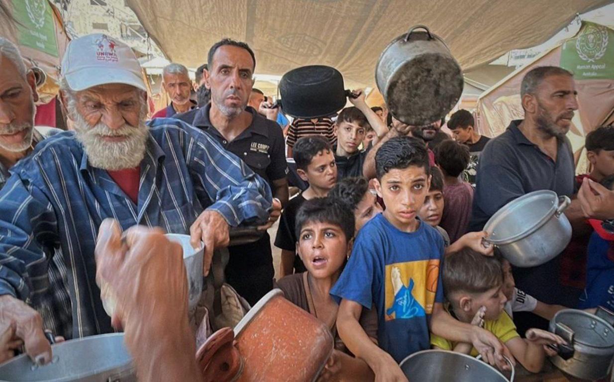 Elderly man and children in Gaza line up for food, receiving aid with pots and pans, supported by crypto donations in BCH.