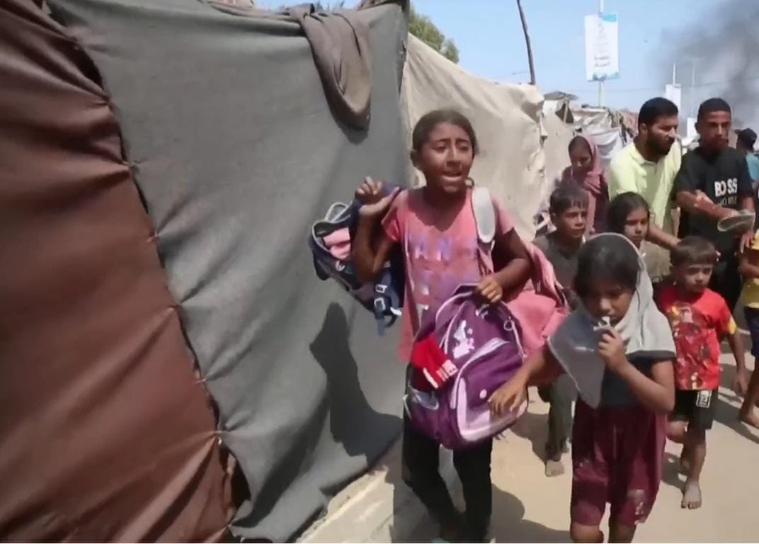 Children carrying backpacks walk past tents in a camp, evoking the need for crypto Zakat donations like USDT to provide aid.