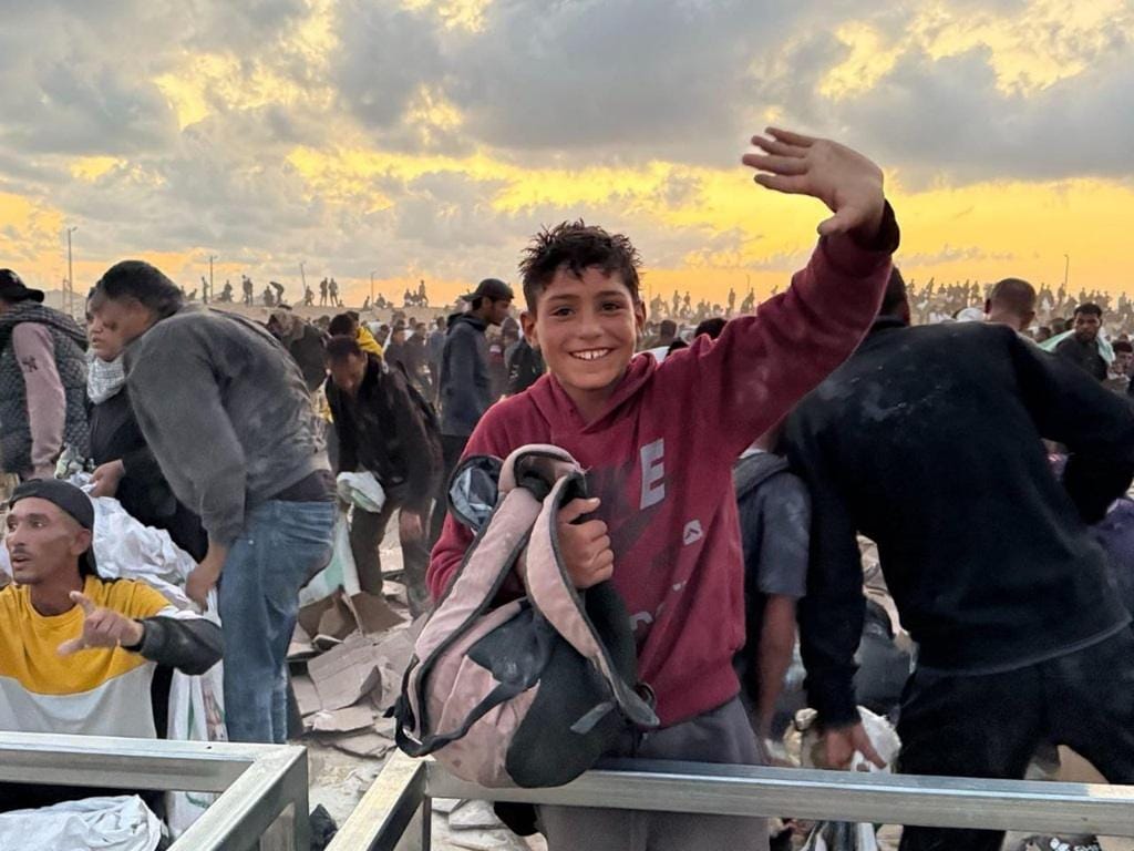 Smiling Palestinian boy waves amidst a crowd, symbolizing hope supported by crypto Zakat donations via Dogecoin, highlighting aid for struggling communities. Keywords: Zakat, Palestine, crypto donation, aid, hope.