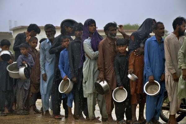 People carrying empty bowls in the rain, receiving aid for the India-Pakistan conflict, with donations possible via SOL.