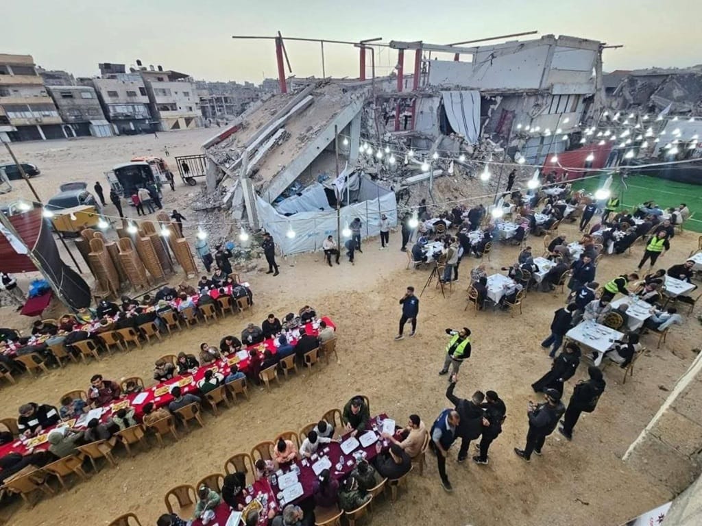 Ramadan Iftar tables are set amidst destroyed buildings in Gaza. People sharing meals under string lights. Aid for Palestinian fasters, donate via Bitcoin.