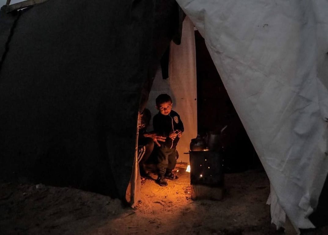 Children huddle inside a tent near a wood-burning stove, receiving warmth and aid through charitable donations received via crypto like ETH.