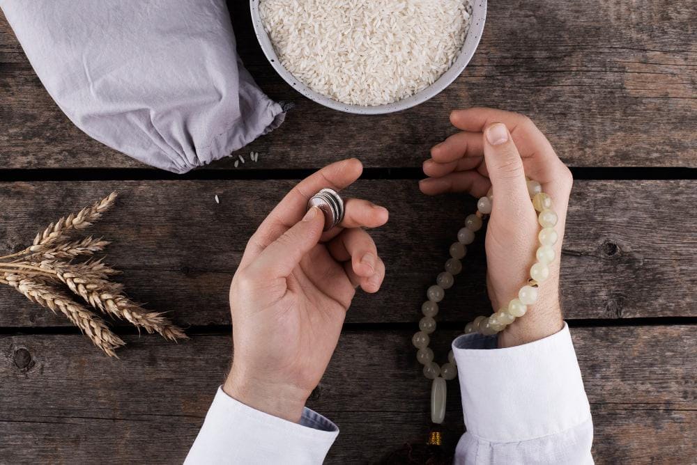 Hands holding coins and prayer beads, with rice and wheat stalks, representing Zakat donation via cryptocurrency like BTC.