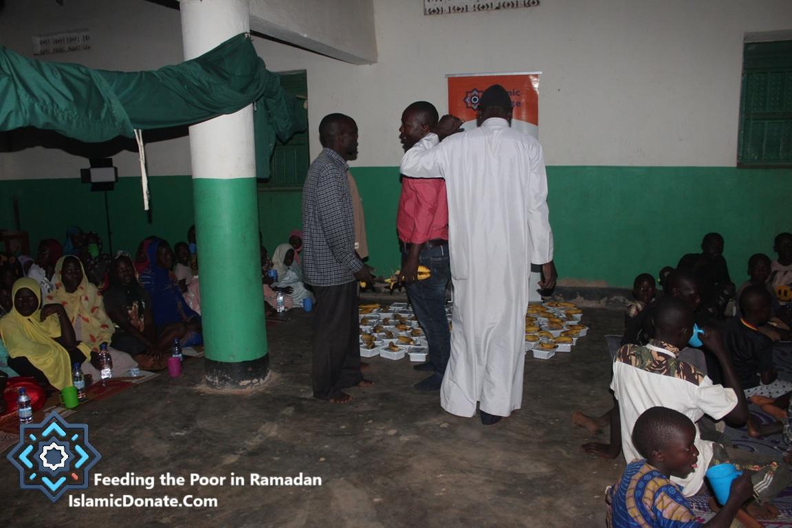 Pay Kaffarah Online and feed poor people with LTC. Volunteers serve hot meals and bananas to families in a communal hall.