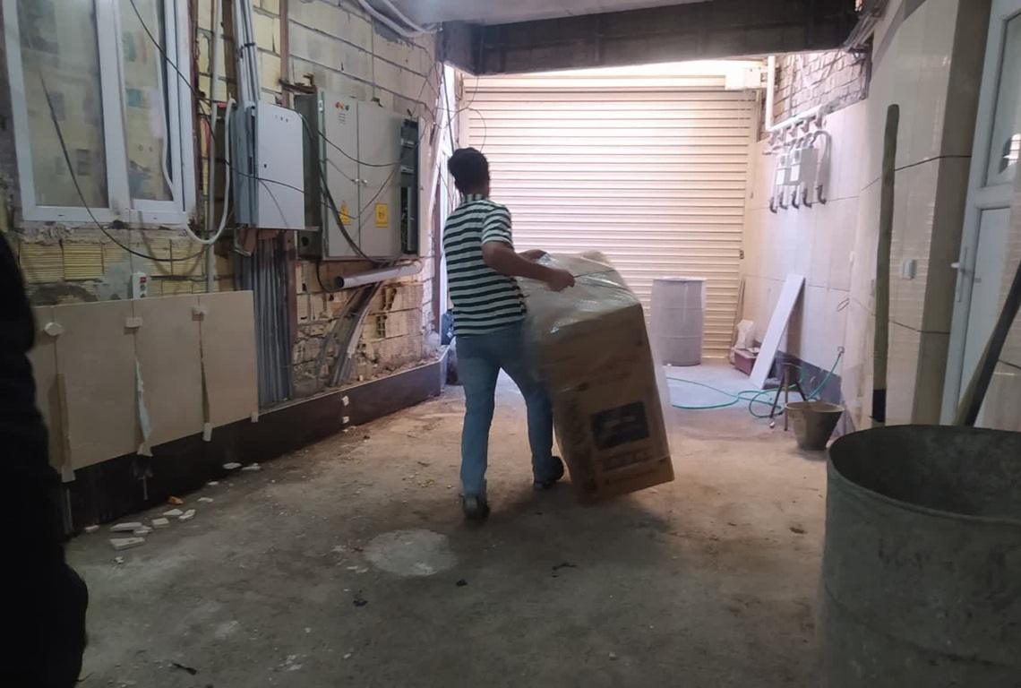 Person carrying a large, wrapped box through a back alley. This image relates to urgent refugee needs, showcasing the logistics of delivering aid like food and water, supported by crypto donations such as ETH.
