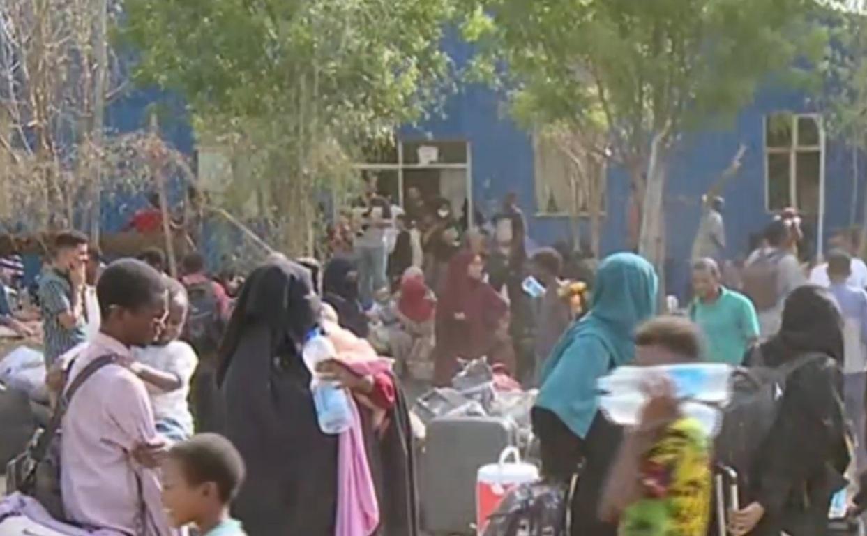 Crowd of displaced people with luggage, seeking humanitarian aid in Sudan and South Sudan, with crypto donations supporting relief efforts via Bitcoin.