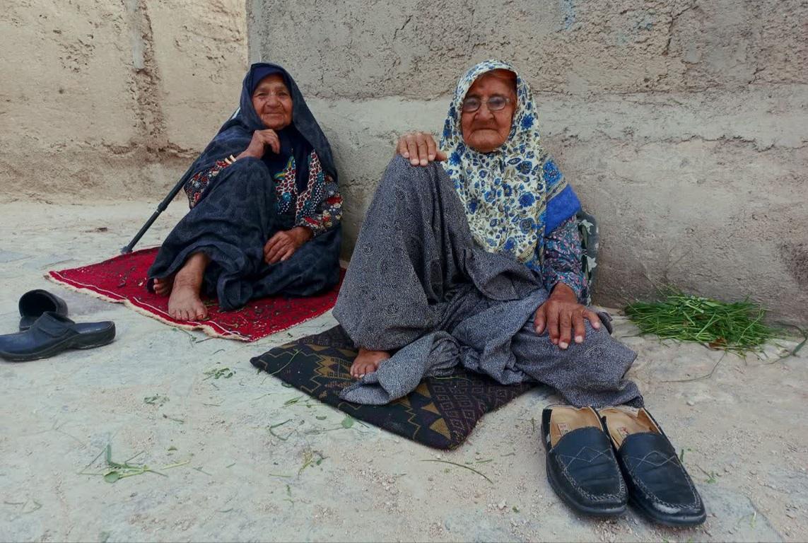 Two elderly women sitting on rugs outdoors, one holds a cane. This image represents the charitable work of Islamic Donate supporting seniors through cryptocurrency via SOL donations.