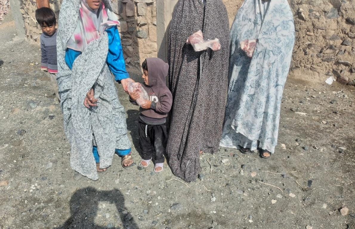 A woman hands a child a package of meat as other women in the background also hold meat packages, distribution of Qurbani or Aqeeqah meat to families in need, made possible through donations potentially via cryptocurrency like Ethereum.
