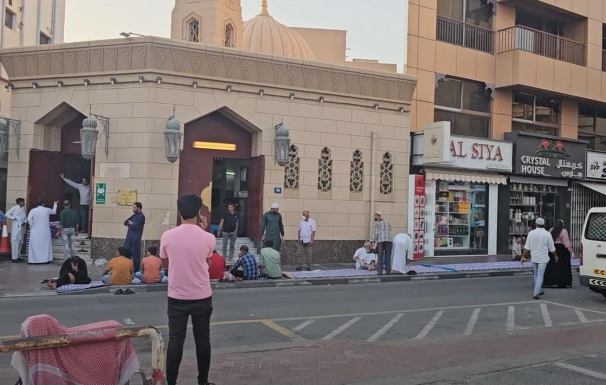 Congregation praying outside a mosque, with some individuals sitting on prayer mats on the street. Reflects the charitable act of donating Qurbani through cryptocurrency, such as SOL.