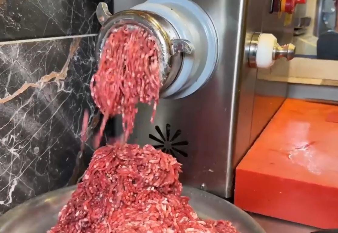 Ground meat exiting a meat grinder, ready for distribution. Supporting Qurbani and Aqeeqah donations with litecoin cryptocurrency for Islamic charity.