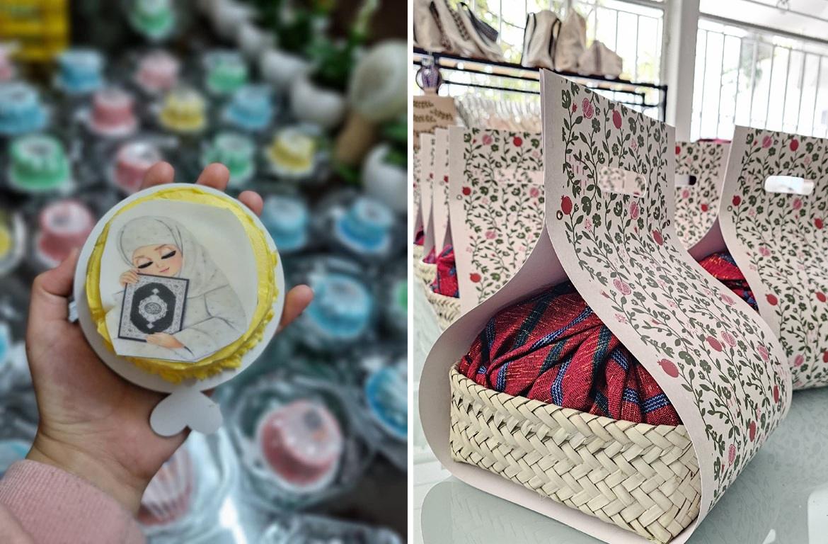 A hand holds a small cake decorated with a drawing of a veiled girl holding the Quran, with rows of colorful mini cakes blurred in the background. Next to it is a woven basket filled with patterned fabric inside a floral gift box, showcasing charitable giving with crypto like Dogecoin.