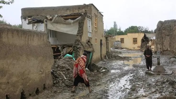 Damaged homes in Afghanistan with people walking through mud, symbol of need for humanitarian aid and crypto donations via USDT.