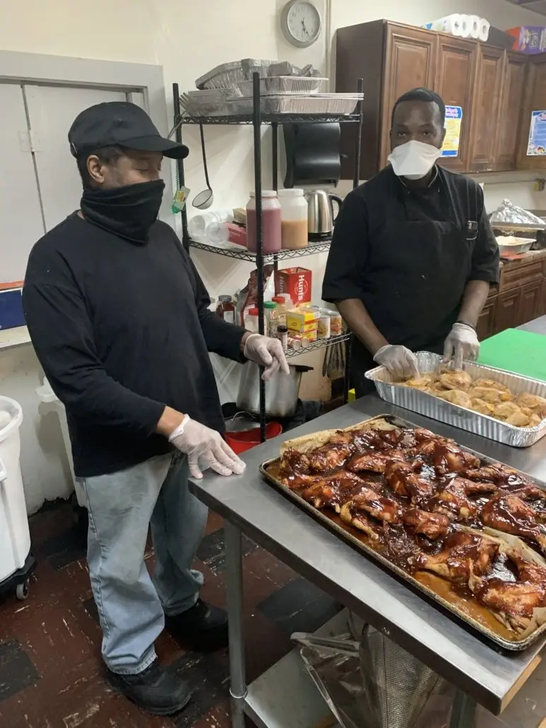 Two chefs with masks and gloves preparing trays of cooked chicken for donation. Crypto donations fund this hot meal program, providing borderless support and fast, efficient aid, powered by ETH.