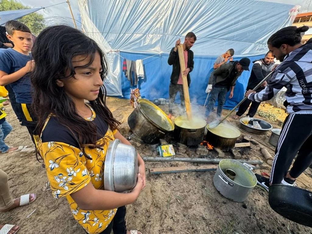 Girl waits for food from soup kitchen at camp while supporting Palestine relief with GRAM alms donation for displaced families.