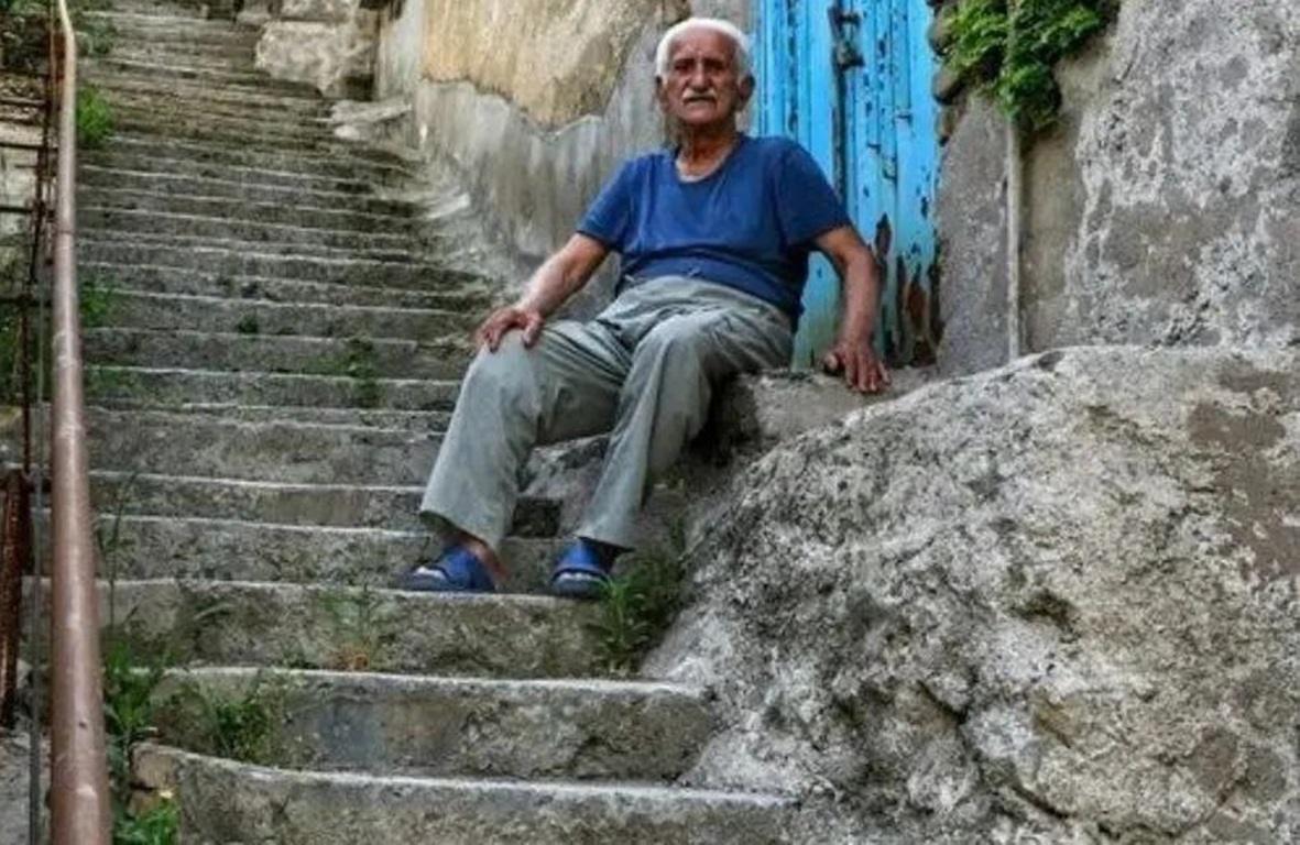 Elderly man sits on worn stone steps, representing those unable to fast; crypto donations of SOL support fidya for needy families.