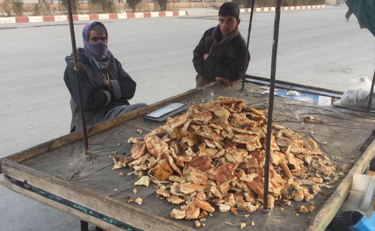 Two individuals beside a cart piled high with bread, likely a street vendor selling food staples. Fidya payment for Ramadan fasting can feed the needy via crypto donations like Monero.