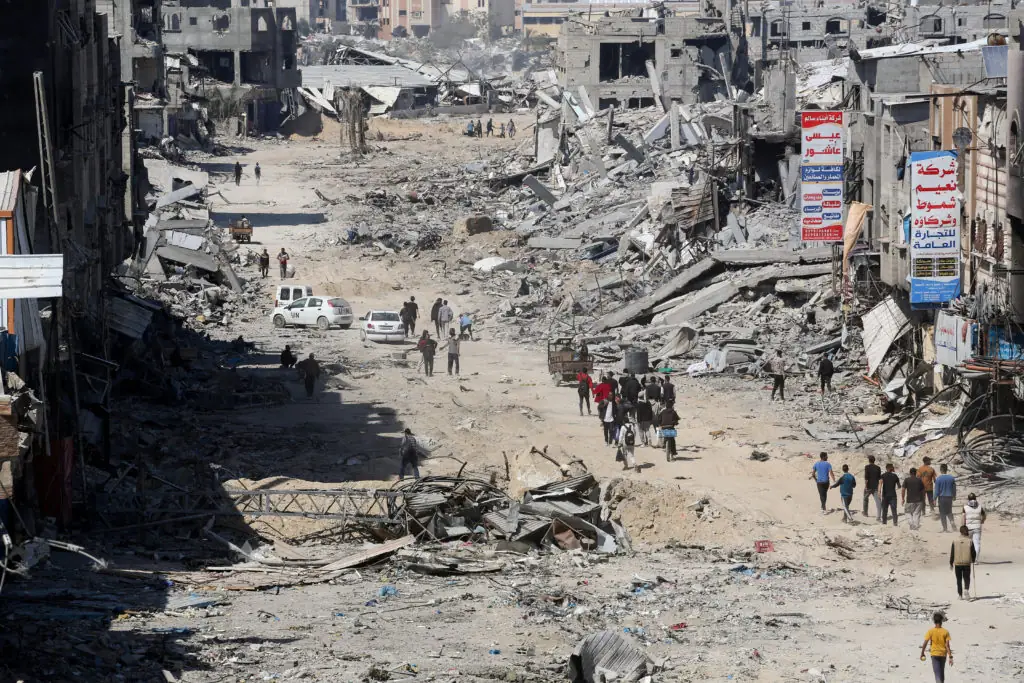 Devastated street in Khan Yunis with rubble and damaged buildings, people walk through the debris. Crypto donation with USDT for urgent humanitarian needs in Rafah and Khan Yunis.
