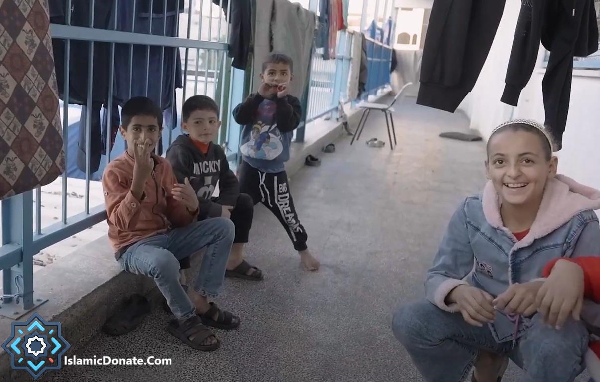 Four children sitting and standing, with one young girl smiling at the camera, posing near laundry hanging on a line. This scene represents support for Muslim orphans, facilitated by crypto donations like ETH.