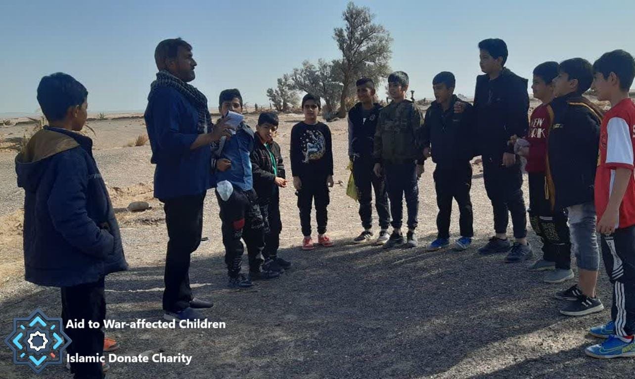 Children gathered around an adult in a desolate area, receiving aid. Aid to War-affected Children, Islamic Donate Charity. Donate with USDT