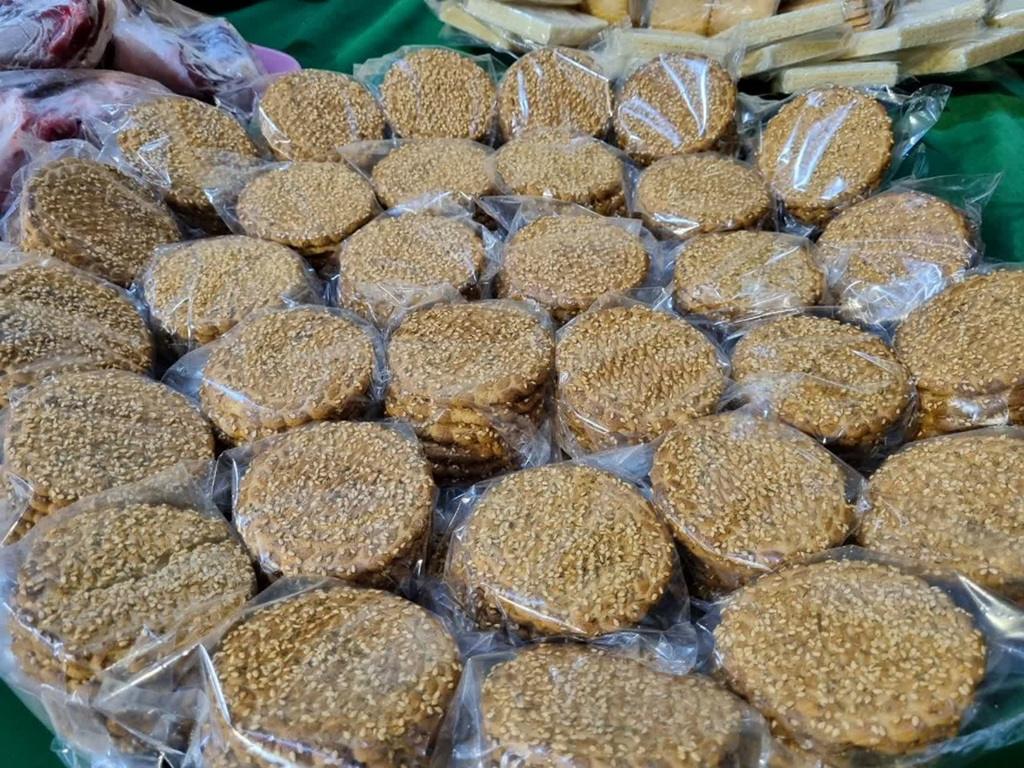 Stacks of round, sesame-seed-covered pastries individually wrapped in clear plastic, presented for charity during Mawlid celebrations. Donate with USDT.
