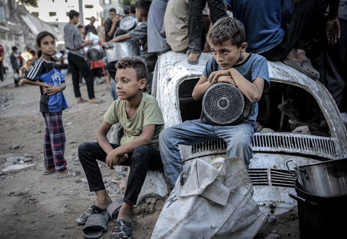 Displaced children in Gaza wait for food aid near tent camps as relief arrives via Arbitrum aid.