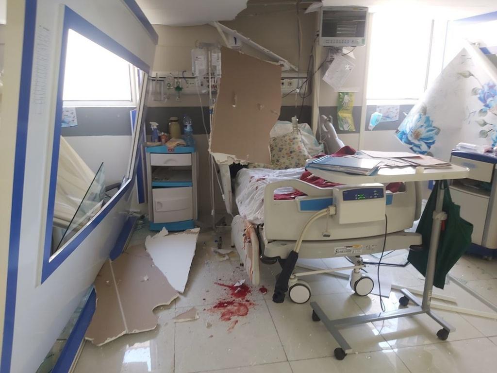 Damaged hospital room in Tehran due to war, showing shattered walls, an overturned medical cart, and a hospital bed splattered with blood. The destruction highlights urgent needs for aid, supported by fast cryptocurrency donations like Bitcoin.