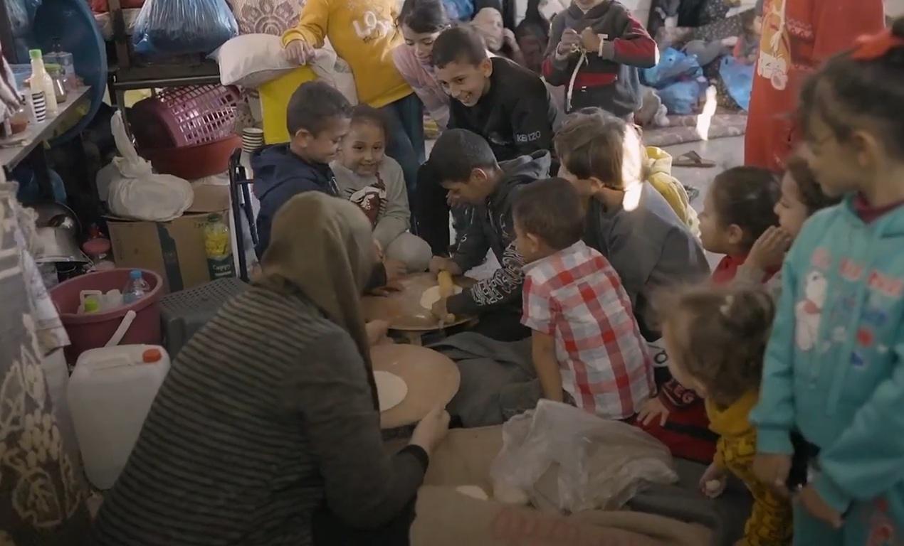 Children learning to make bread with volunteers in a crowded shelter in Gaza, supported by crypto donations like BTC.