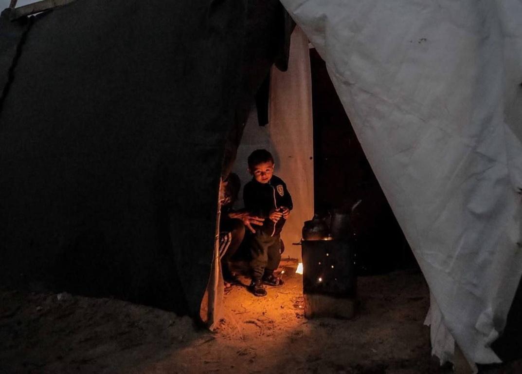 Children huddle inside a tent near a wood-burning stove, receiving warmth and aid through charitable donations received via crypto like ETH.