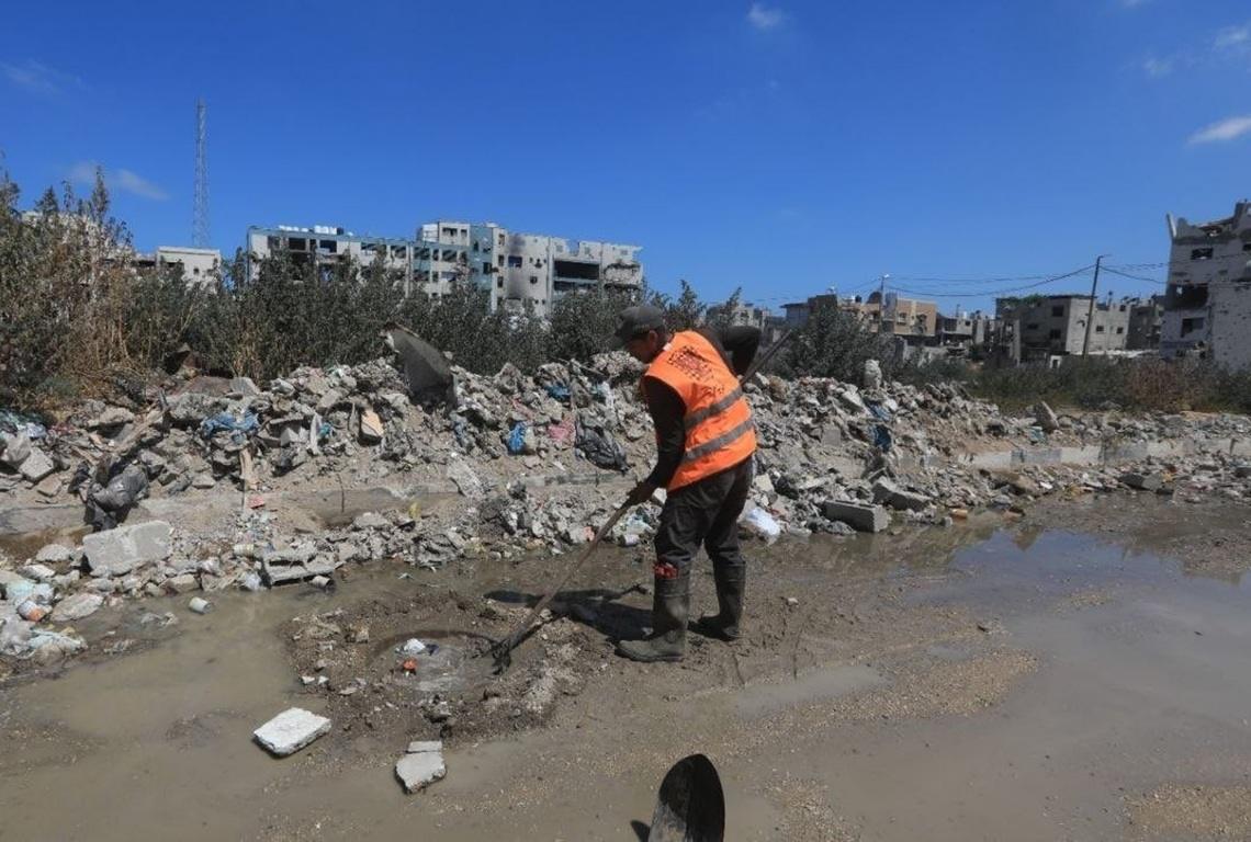 Sanitation worker cleans stagnant sewage in Gaza to prevent disease hazards funded by Dogecoin and charity crypto donations.