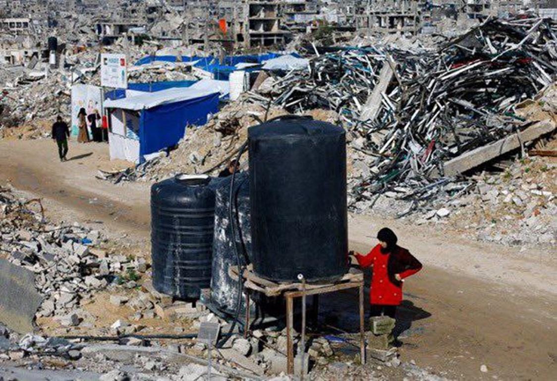Clean water tanks amidst Gaza rubble prevent disease hazards. Help Gazans in heat by donating Bitcoin for hygiene and medication.