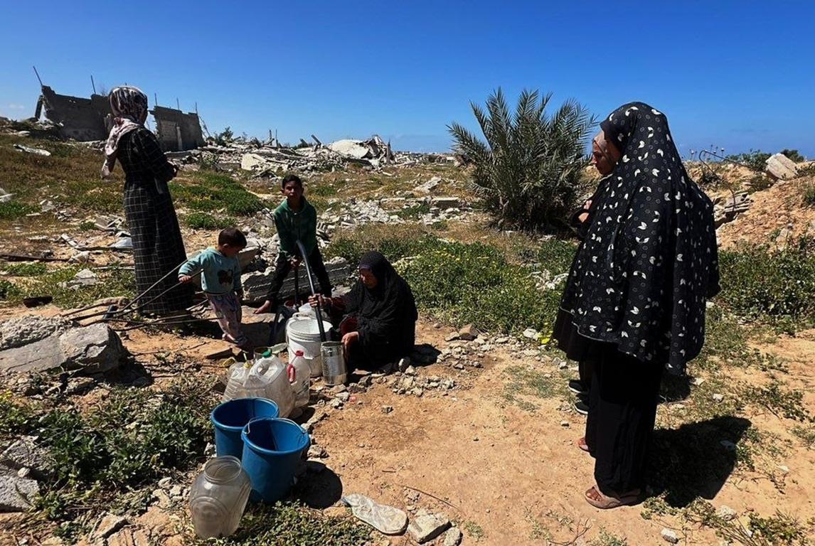 Gazan families collect clean water near rubble to fight disease in heat using PAXG donations for hygiene and survival.