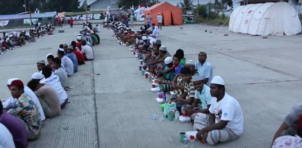 Muslims sit in rows to receive Iftar meals, with food packages and sustenance provided by donors, including crypto contributions like LTC.