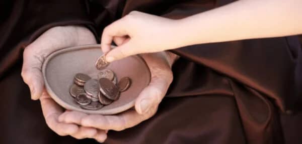 Close-up of wrinkled hands holding a bowl, with a child's hand dropping a coin. This depicts giving Sadaqah with crypto, symbolizing daily charity for hot meals, debt relief, and support for orphans, enabled by ETH.
