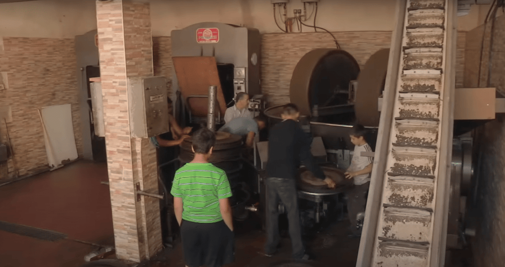 Syrian workers operating machinery in a restored olive oil workshop, receiving crypto donations for sustainable livelihoods via Ethereum.