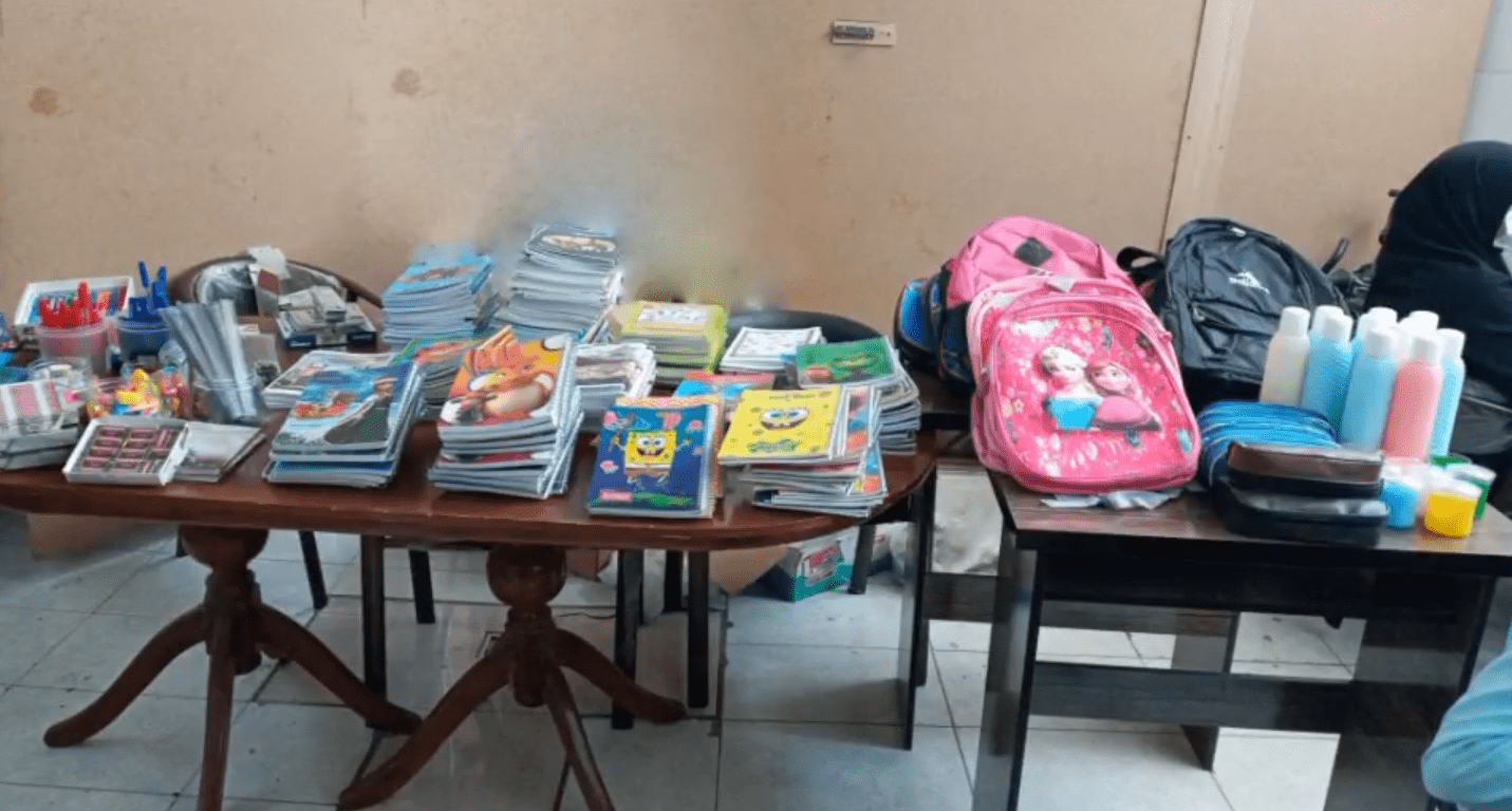 Back to School Report 2024: Piles of notebooks, pencils, and school supplies including backpacks and bottles of sanitizer, ready for distribution to sponsored orphans, made possible by crypto donations like BTC, fostering education and potential.