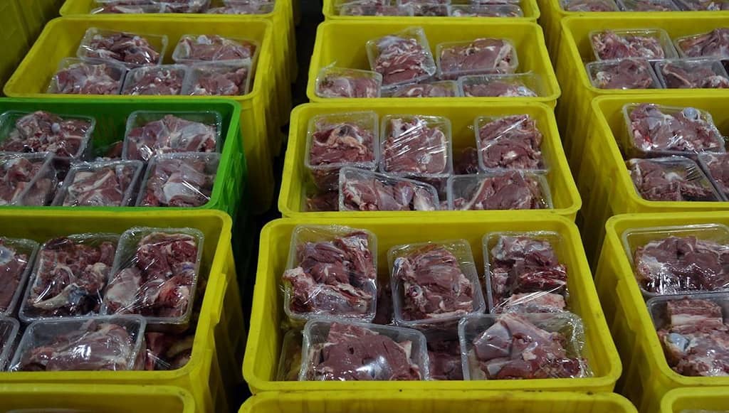 Rows of yellow bins filled with pre-packaged raw meat portions, ready for distribution as Eid al-Adha charity, supported by USDT donations for sustenance relief.