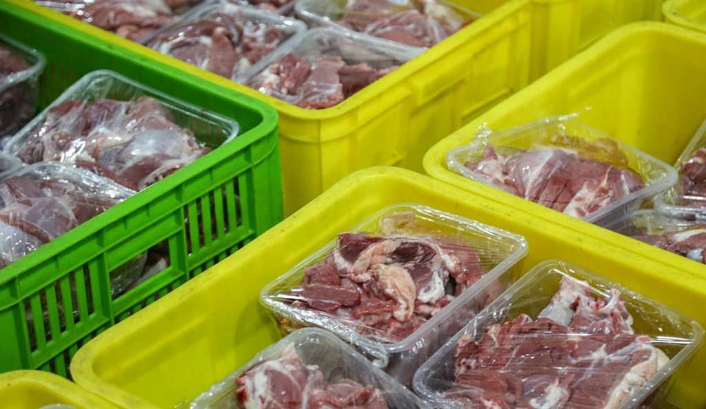 Eid al-Adha 2024 meat distribution featuring raw meat packages in crates, supported by Arab Emirates Dirham donations for humanitarian aid.