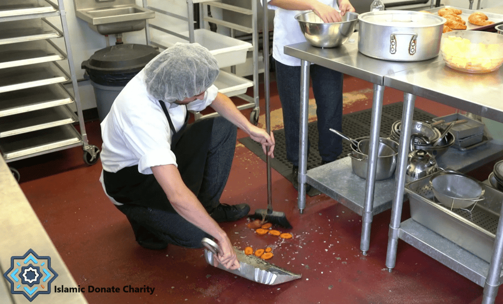 A volunteer cleans a kitchen floor where chopped carrots have fallen, symbolizing the essential but often unseen work of charitable operations funded by crypto donations like BTC.