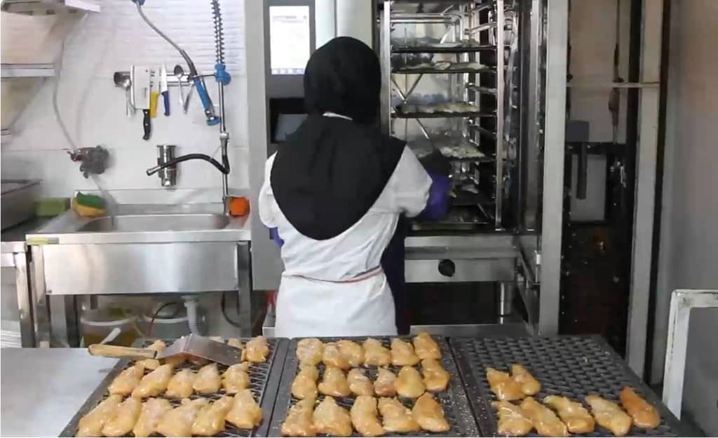 A cook in a hijab prepares food for the needy at a soup kitchen, likely supported by BTC donations, serving the Muslim Ummah with dedication and faith.