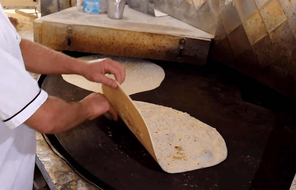 A baker prepares fresh bread on a large, circular griddle, symbolizing hope and sustenance for Palestine, with donations enabling cryptocurrency contributions like BTC.